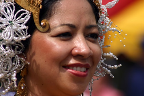 A person is wearing a traditional headpiece adorned with intricate white beadwork and gold embellishments, smiling warmly.