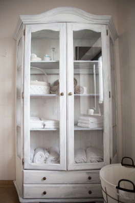 Tall drawer linen tower filled with soft towels in a sunlit bathroom corner.