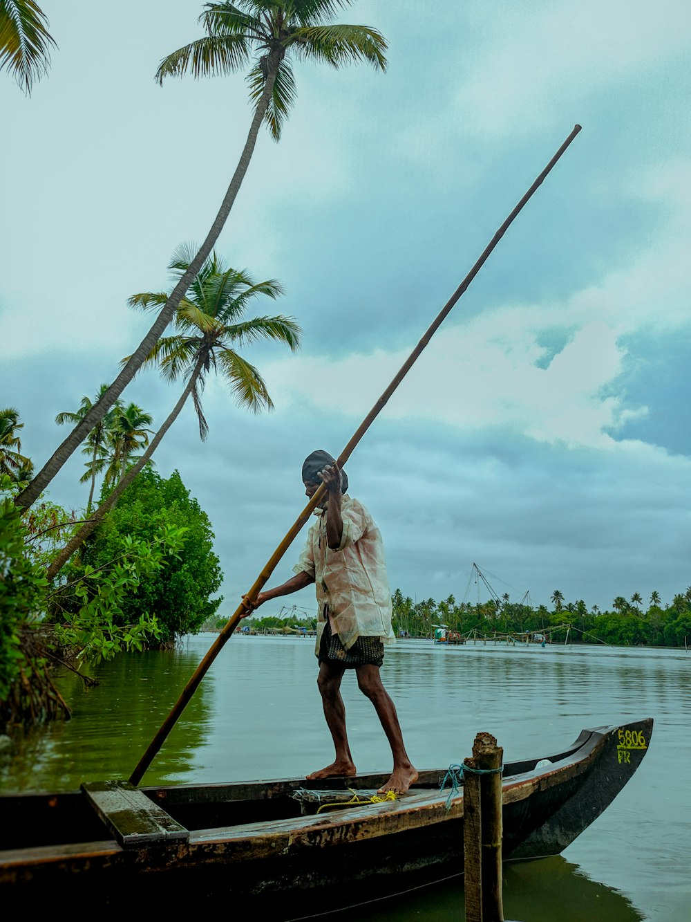 man in white shirt and brown shorts on brown wooden boat on body of water during