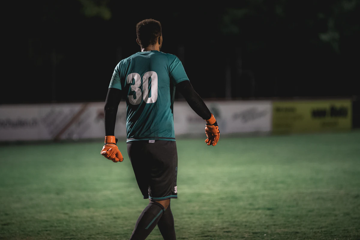 A goalkeeper walks back to his goal under the floodlights