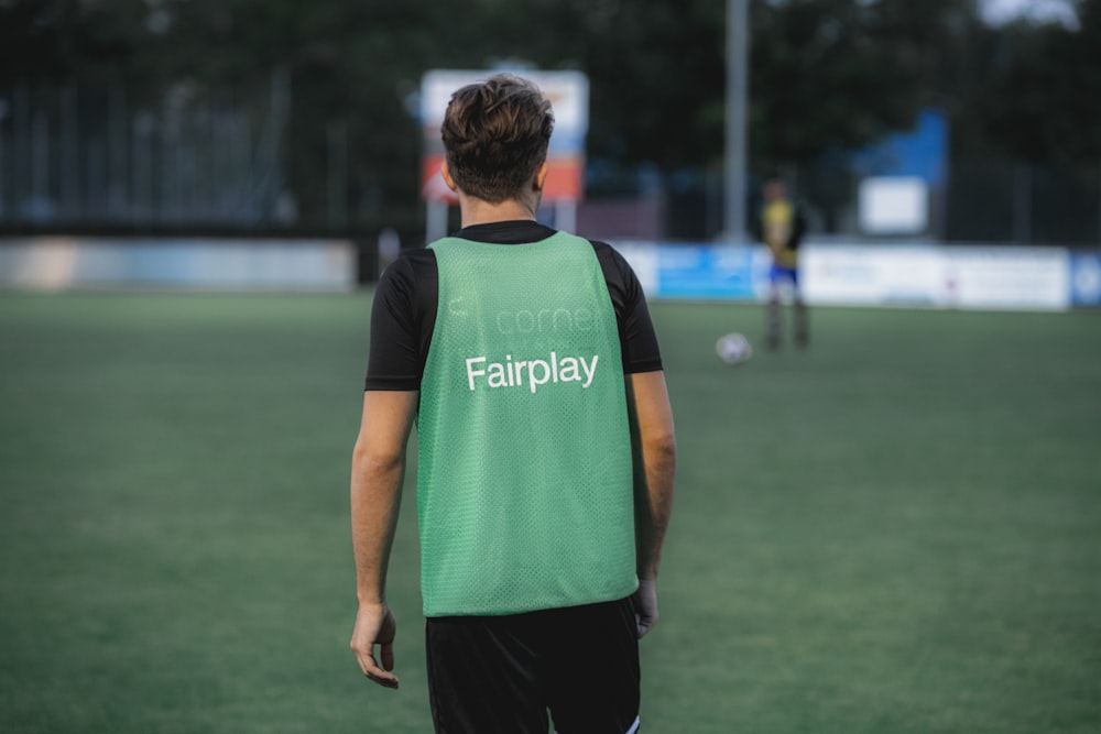 Hombre con camiseta sin mangas adidas verde y negra y pantalones negros de pie en un campo de hierba verde