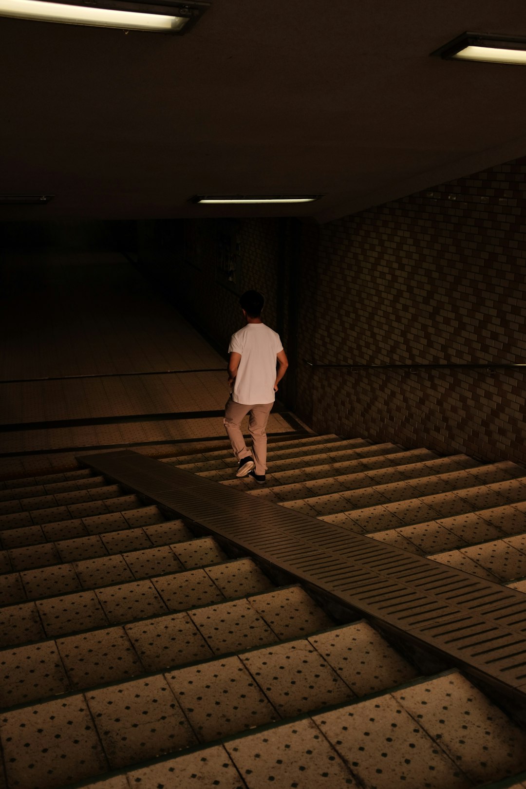 man in white t-shirt and black pants walking on brown wooden stairs