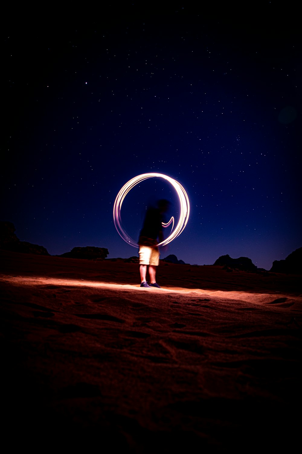 person in white shirt and blue denim jeans standing on brown sand under starry night