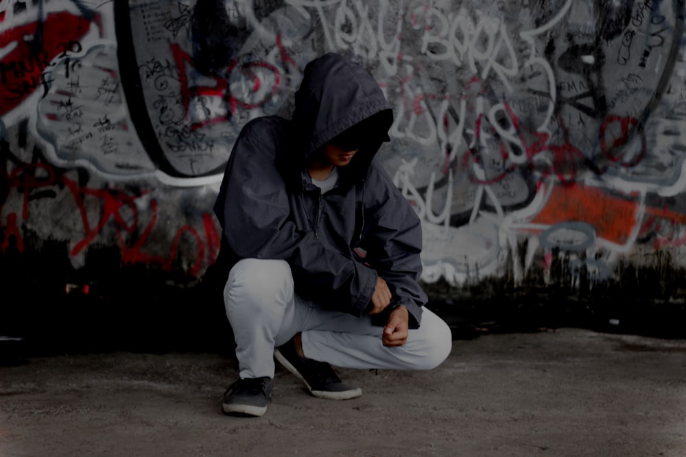 man in black hoodie and white pants sitting on gray concrete floor