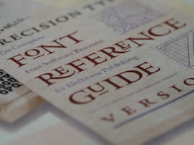 A close-up view of a document featuring the text 'FONT REFERENCE GUIDE' in large, bold, red letters. The background includes a subtle, textured pattern along with smaller text that appears to relate to typography.