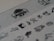 A series of small, detailed black and white illustrations on a textured paper. The images include various objects and symbols, such as a weather vane with a rooster, a tree, and scales, accompanied by other abstract and recognizable shapes. The paper has a grayish tone, and the illustrations are sharp against the slightly blurred background.