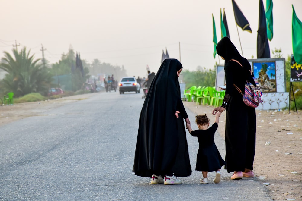 2 femmes en hijab noir debout sur une route asphaltée grise pendant la journée