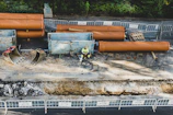 A contractor inspecting drainage pipes on a construction site with tools in hand