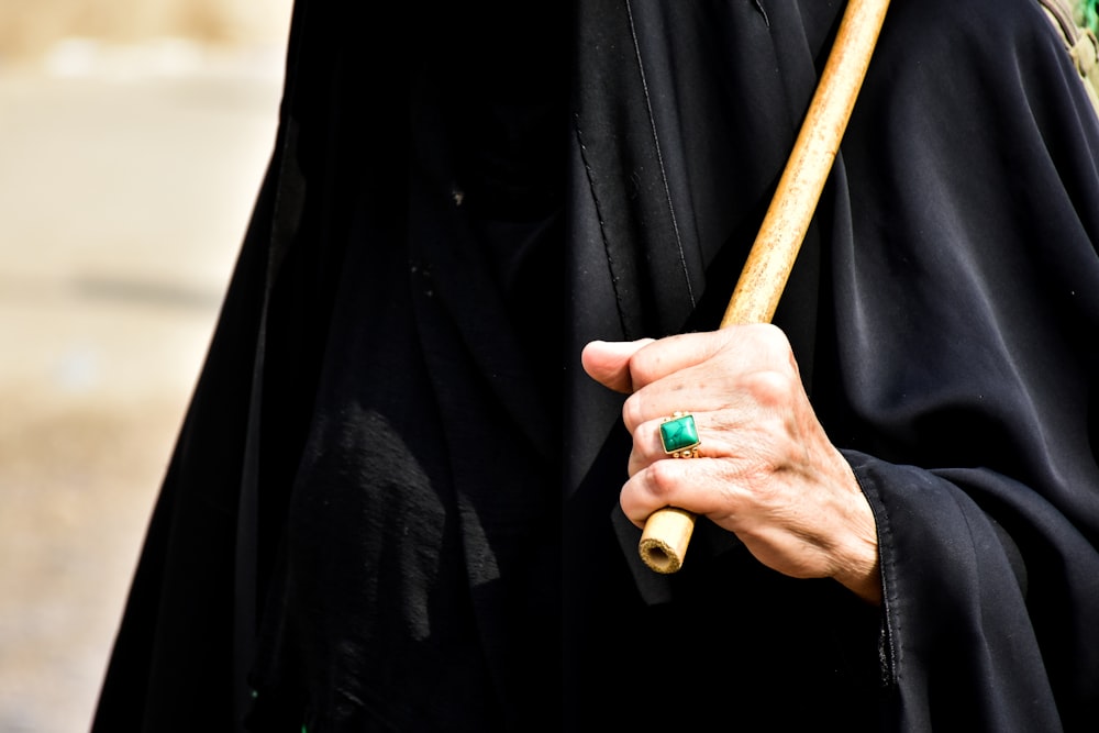 person in black coat holding brown wooden stick