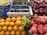 A fruit market display featuring various fruits neatly arranged in crates and baskets. There are bright orange oranges, shiny red apples, deep purple figs, and clusters of green and dark purple grapes. The fruits have a fresh and vibrant appearance, with a sign indicating the price of the grapes.