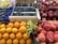 A fruit market display featuring various fruits neatly arranged in crates and baskets. There are bright orange oranges, shiny red apples, deep purple figs, and clusters of green and dark purple grapes. The fruits have a fresh and vibrant appearance, with a sign indicating the price of the grapes.