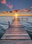 brown wooden dock stretching out over water with sunset in horizon