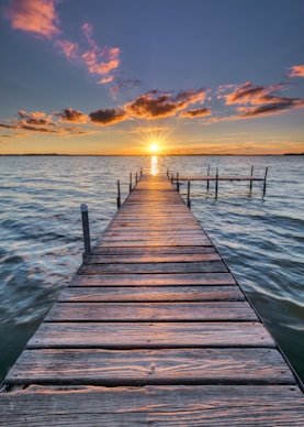 brown wooden dock stretching out over water with sunset in horizon