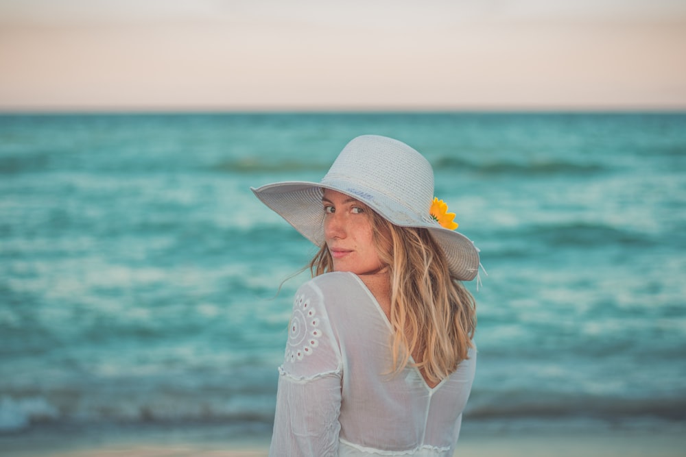 woman in white sun hat and white long sleeve shirt standing on beach shore during daytime