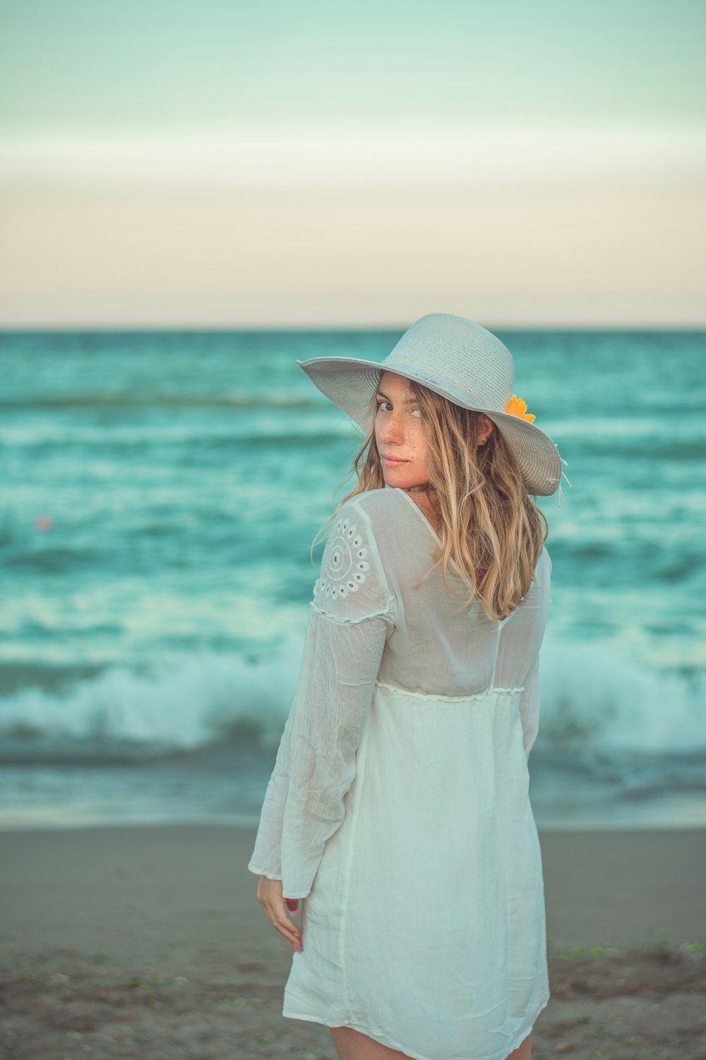 woman in white dress wearing brown hat standing on seashore during daytime