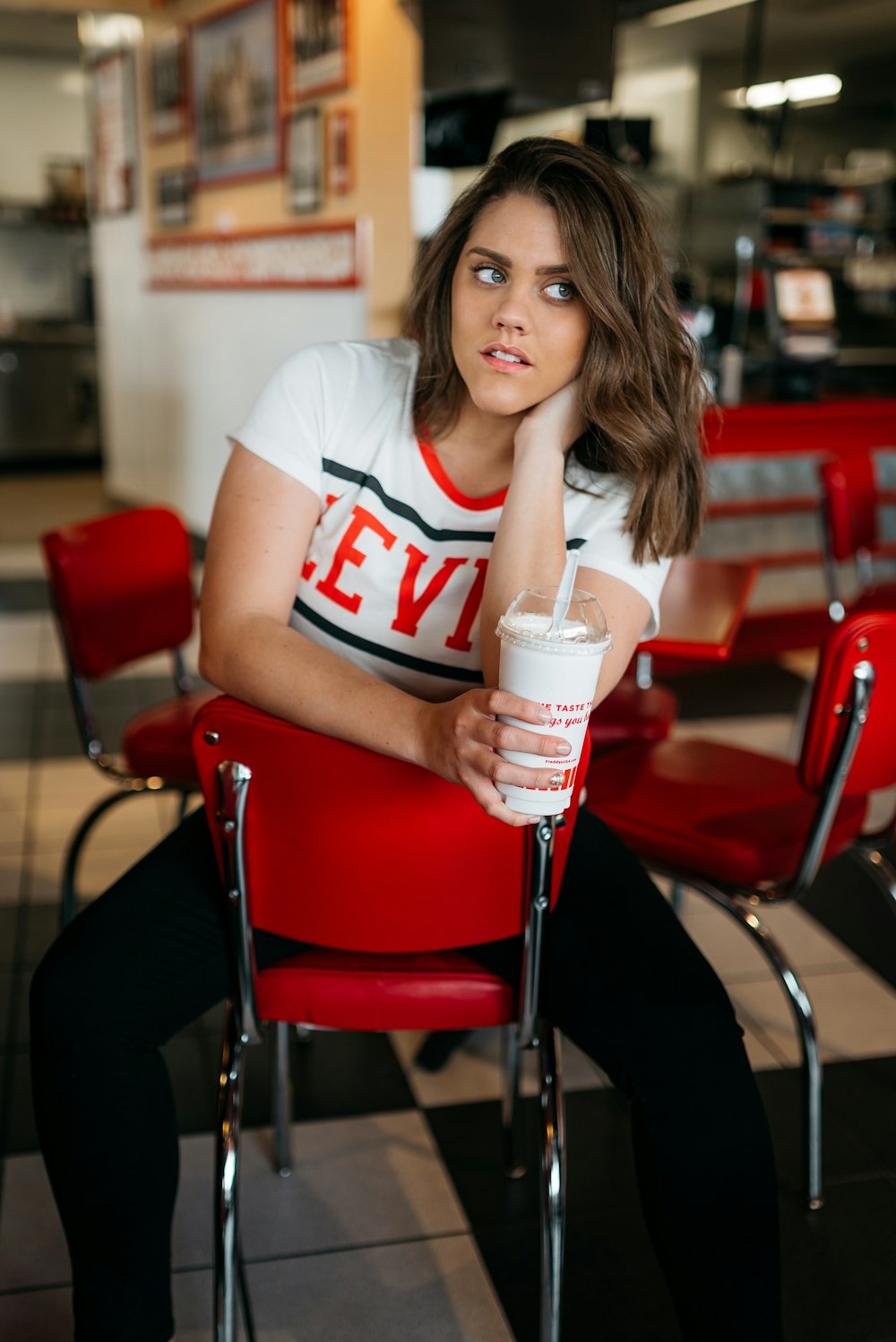 mulher na camiseta branca sentada na cadeira segurando o copo descartável branco