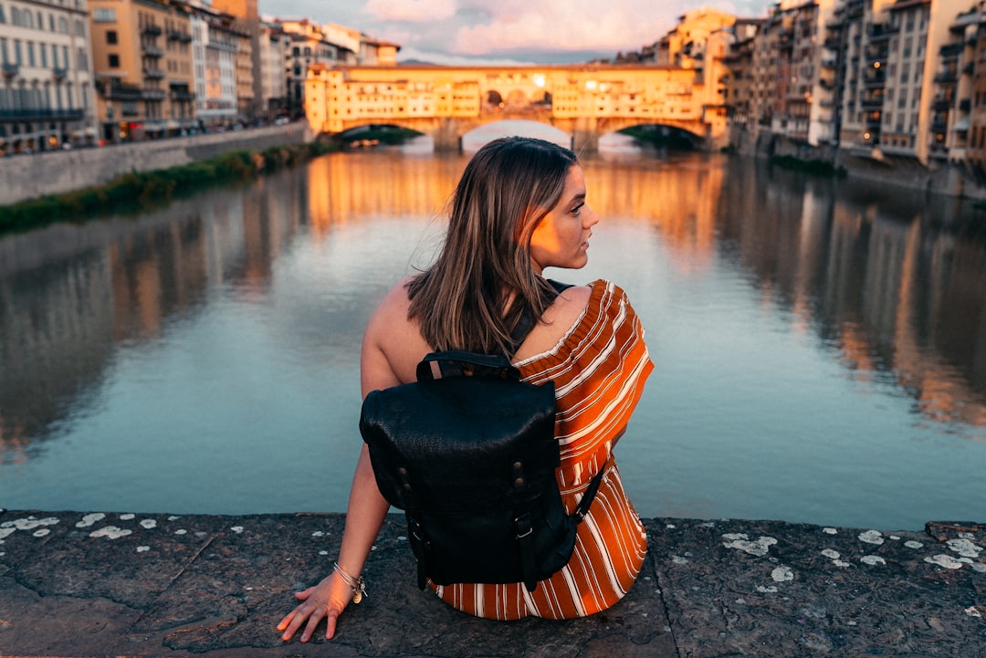 woman in black and orange striped shirt and black leather sling bag standing on gray concrete