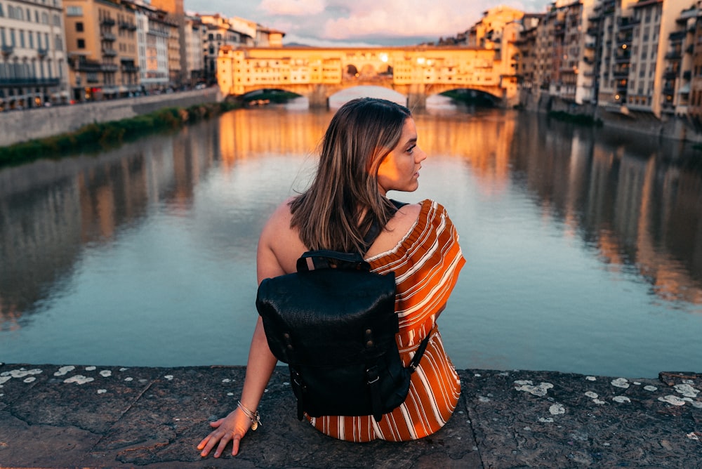 woman in black and orange striped shirt and black leather sling bag standing on gray concrete