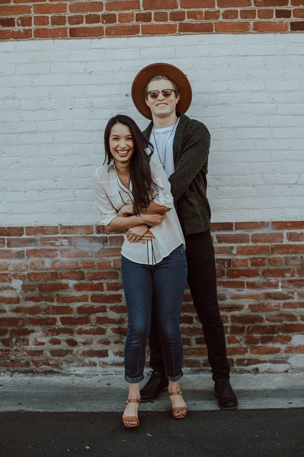 woman in brown coat and blue denim jeans standing beside brown brick wall