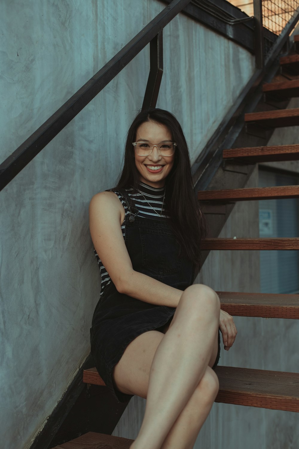 woman in black sleeveless dress sitting on brown wooden staircase