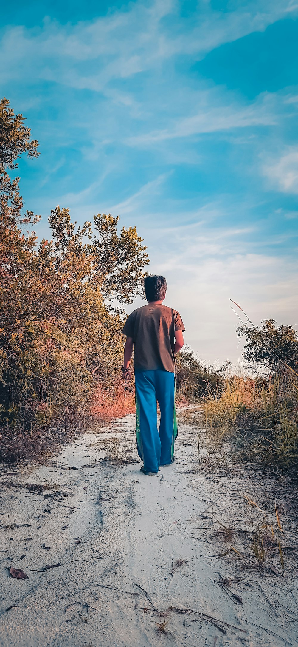 man in brown shirt and blue denim jeans standing on dirt road during daytime