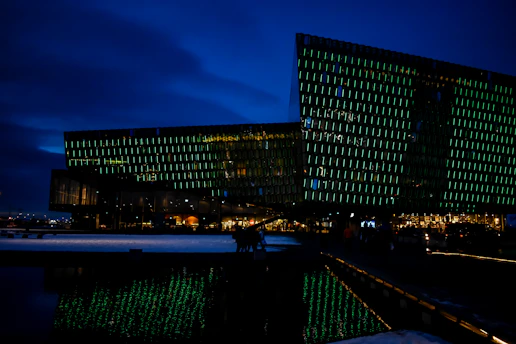 A sleek, futuristic glass building glowing softly with dark-green and white lights, symbolizing innovation and sustainability at the Greenovator Incubation Foundation.