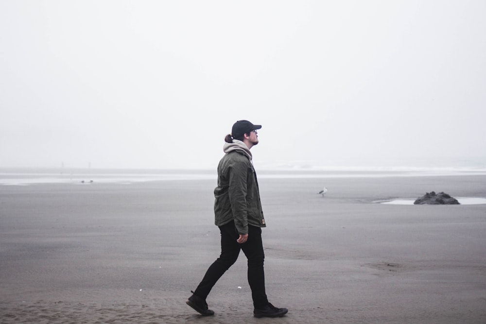 man in gray coat walking on beach during daytime