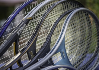 Several tennis rackets are closely positioned together, showcasing their strings and frames. The rackets have various colors and branding, including visible text on some frames.