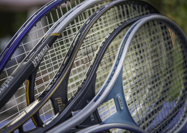 Several tennis rackets are closely positioned together, showcasing their strings and frames. The rackets have various colors and branding, including visible text on some frames.