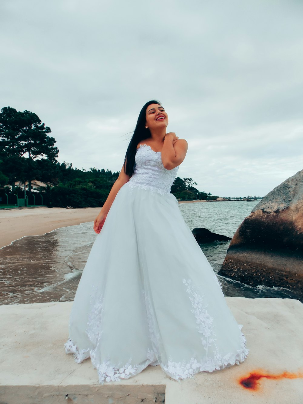 woman in white wedding dress standing on brown sand near body of water during daytime