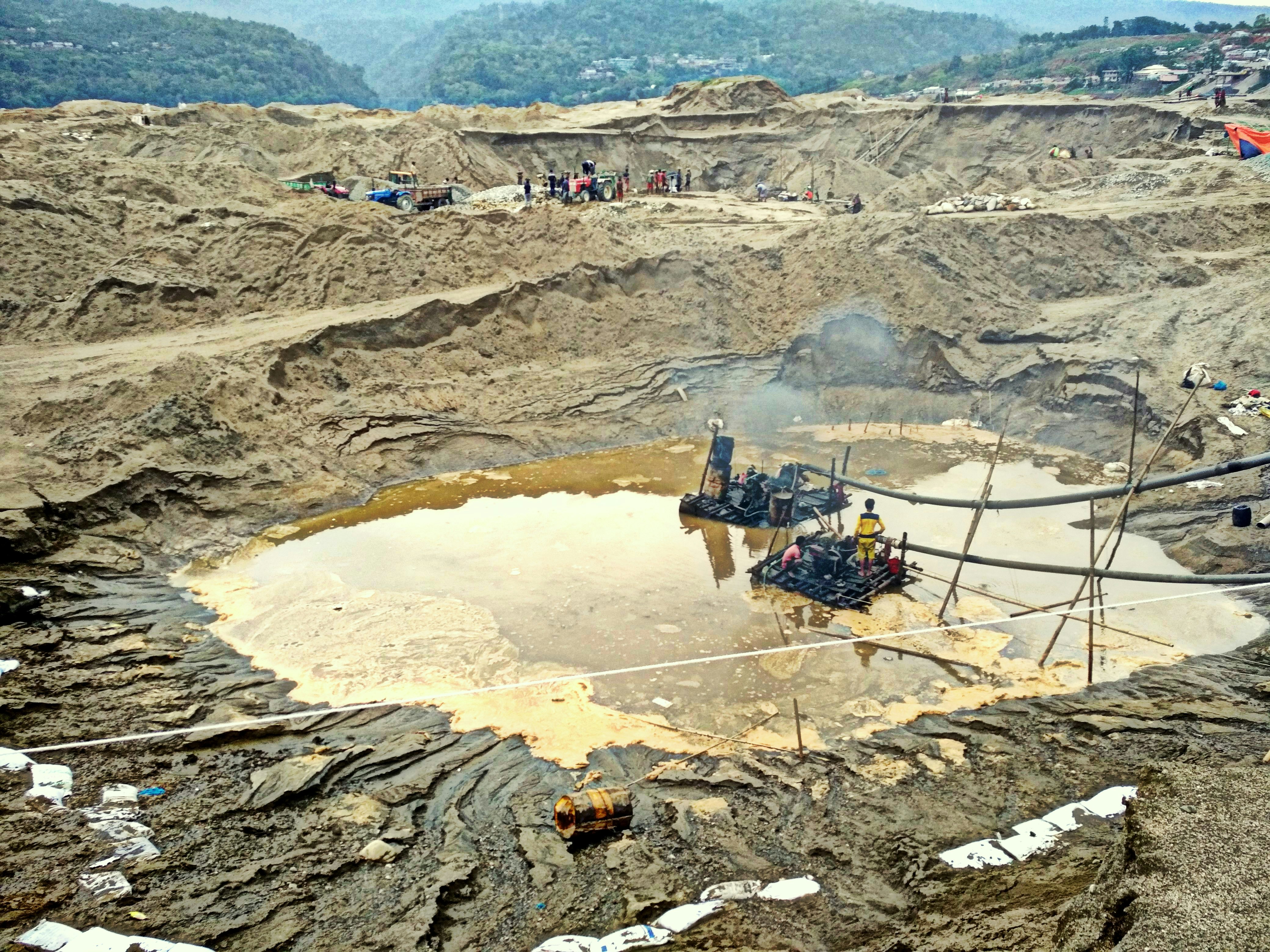 Construction excavation site with groundwater visible, workers operating equipment in open trench