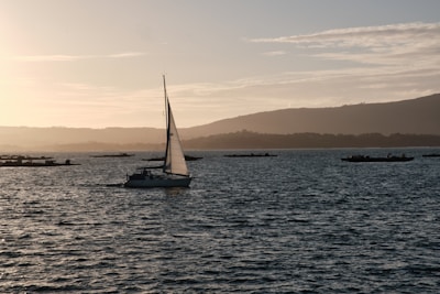 A modern sailboat cruising on calm waters with a sunset in the background.