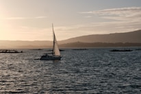 Sailboat navigating calm waters with mountains in the background during sunset.
