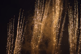 Golden fire shots shooting upward, leaving trails of sparkling light against a deep black backdrop.