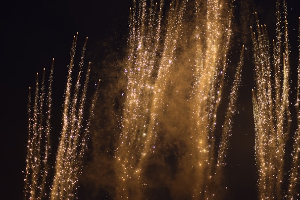 Golden fire shots shooting upward, leaving trails of sparkling light against a deep black backdrop.