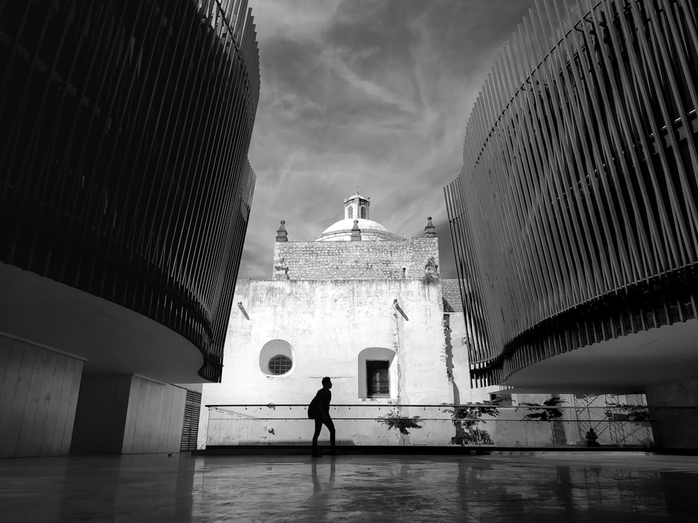 grayscale photo of man walking on sidewalk near building