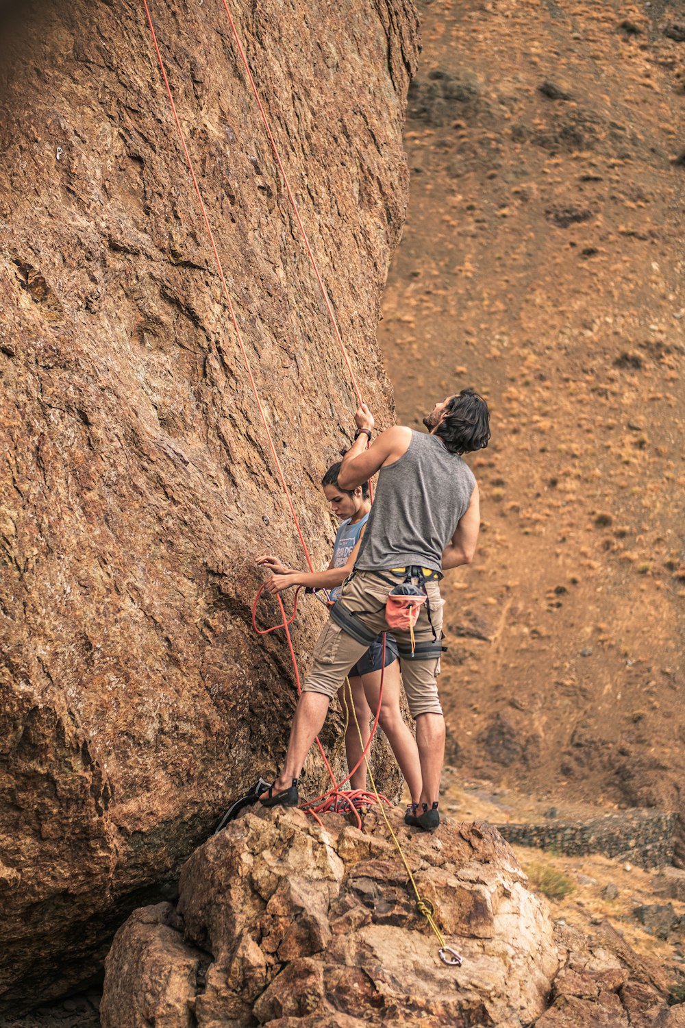 man in gray t-shirt and blue denim shorts climbing brown rock during daytime
