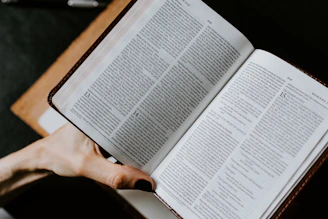 Hands holding an open Bible with light shining on the pages.