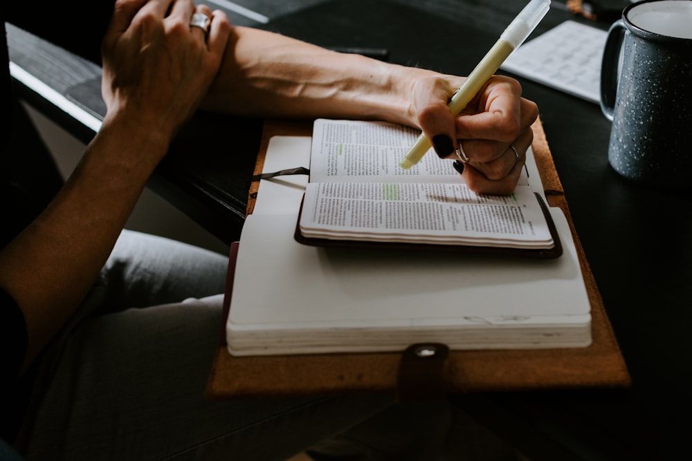 person holding white pen writing on white notebook