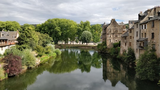 brown concrete building near green trees and river under white clouds and blue sky during daytime in Espalion France