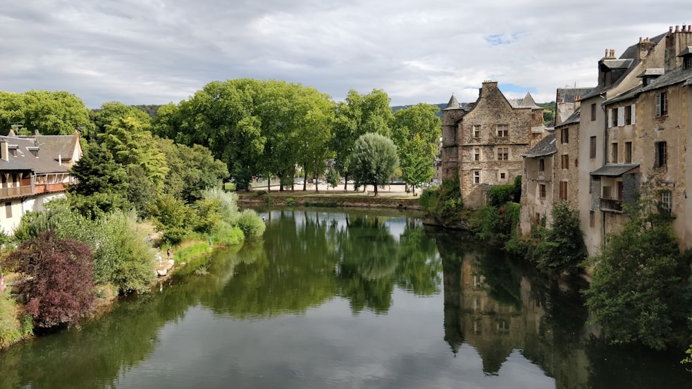 Edificio de hormigón marrón cerca de árboles verdes y río bajo nubes blancas y cielo azul durante el día