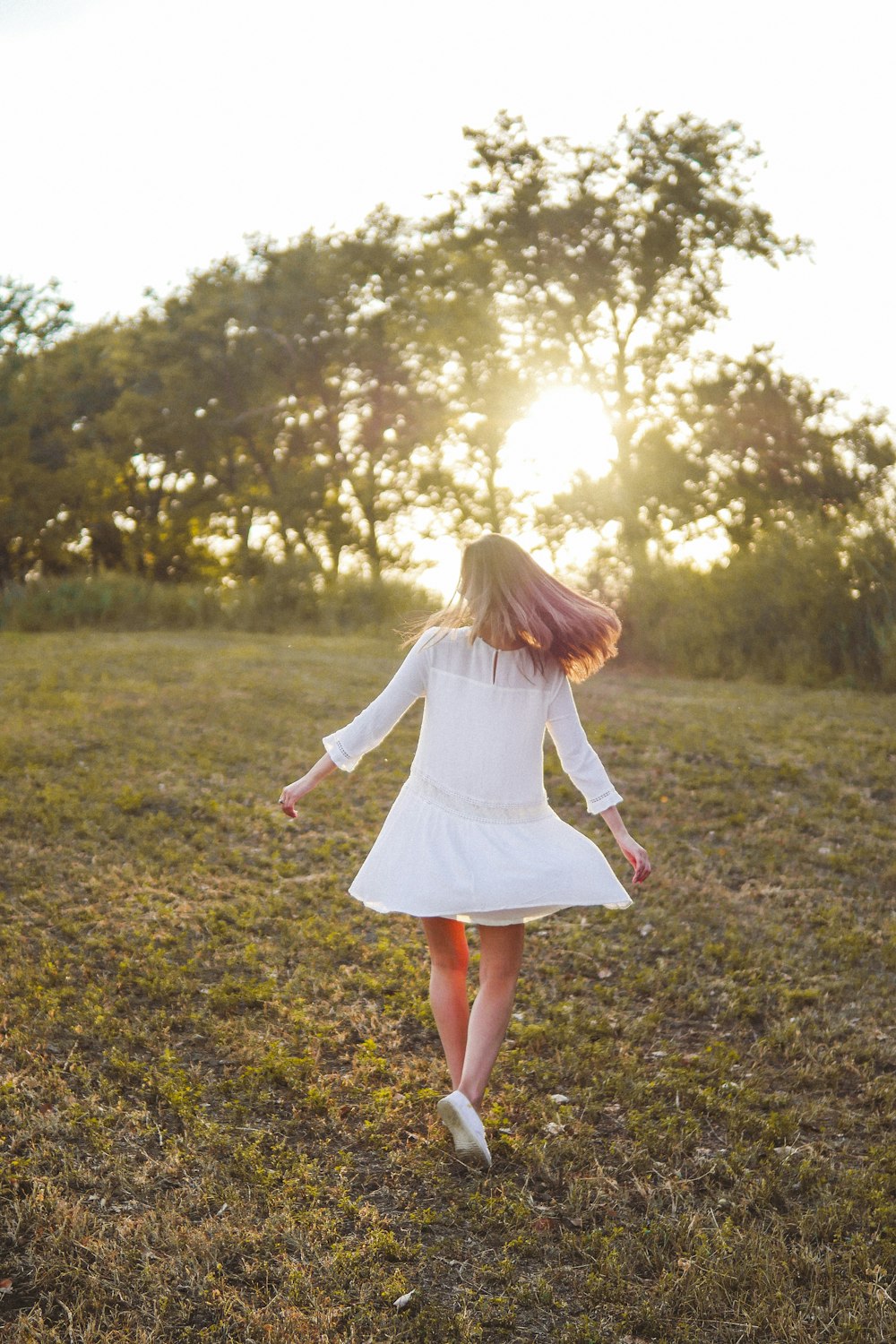 낮 동안 푸른 잔디밭에서 달리는 흰색 긴팔 드레스를 입은 소녀