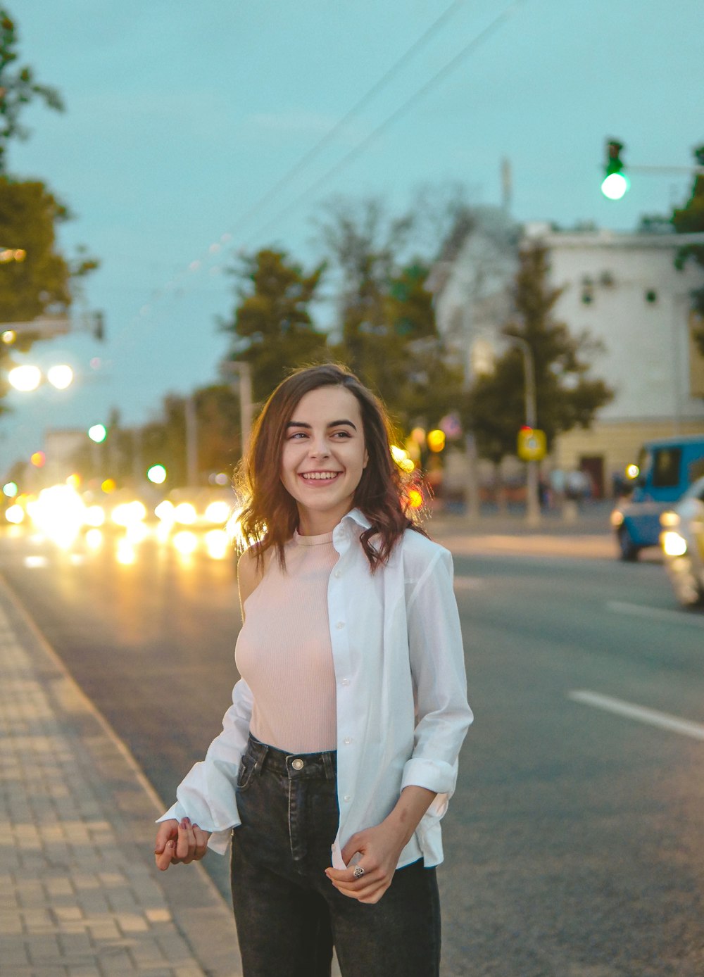 woman in white dress shirt and black denim jeans standing on sidewalk during night time