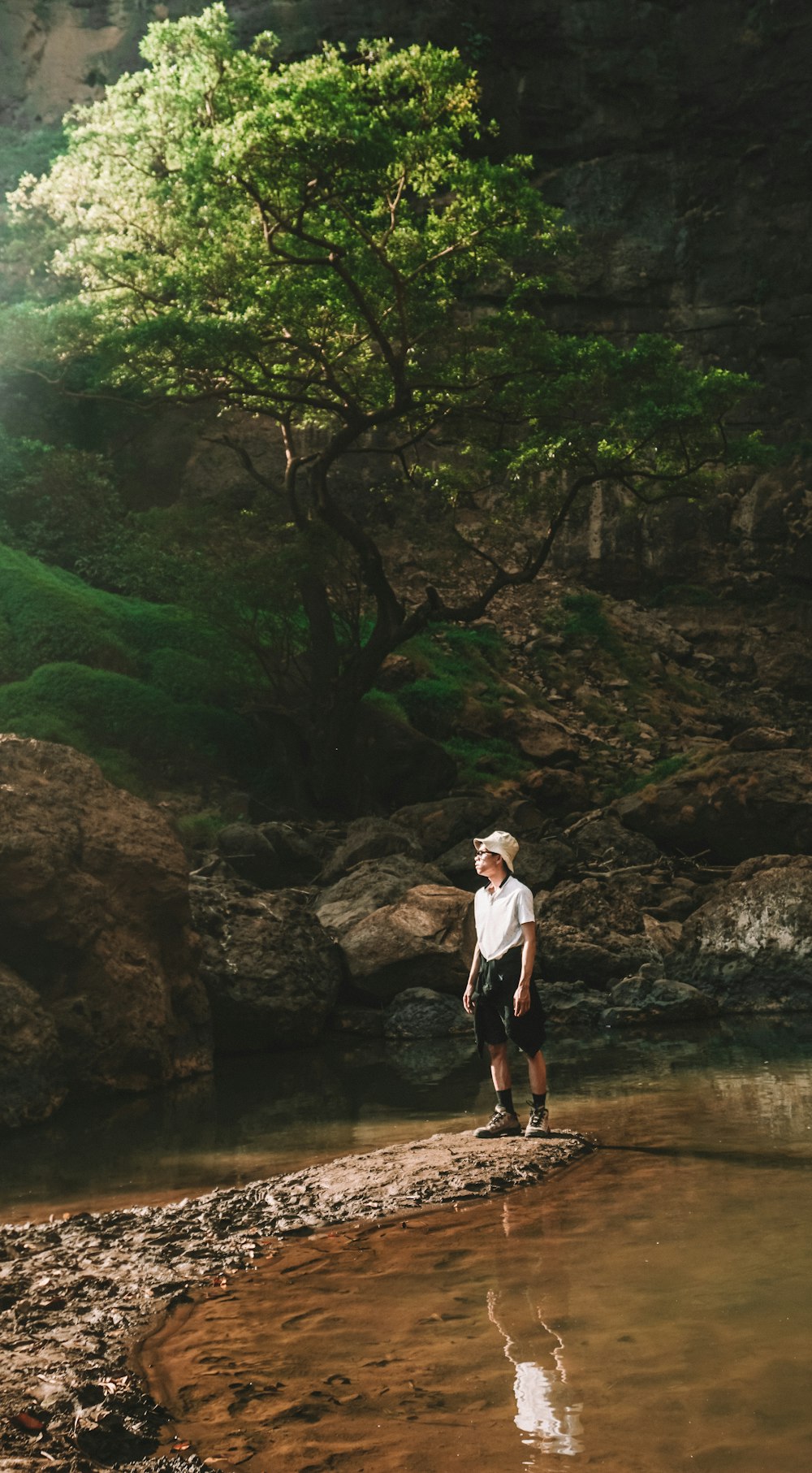 Mann im weißen Hemd tagsüber auf einem braunen Felsen in der Nähe des Flusses