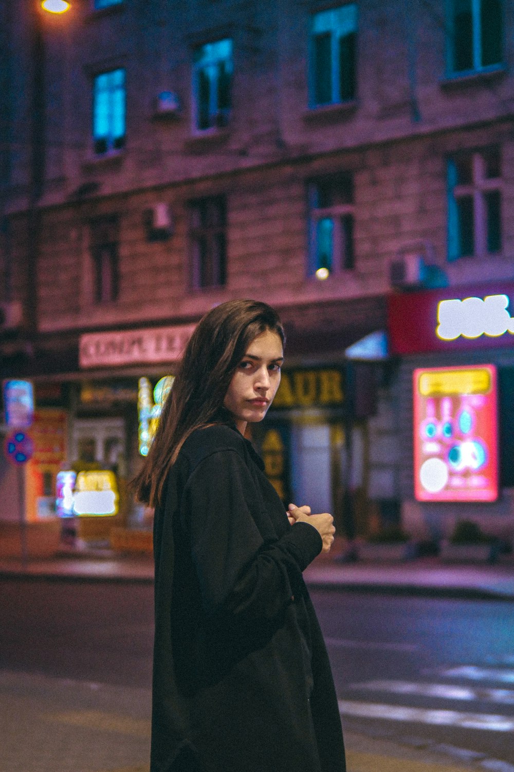 woman in black coat standing near red building during night time