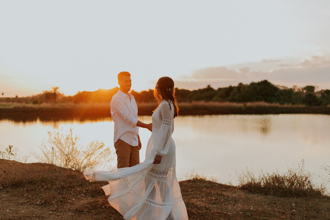 couple standing on brown grass field near body of water during daytime