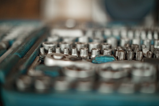 A close-up of a set of metallic socket wrenches and other related tools, arranged in an orderly manner. The tools have a silver finish and are housed in a blue tray or case, partially blurred.
