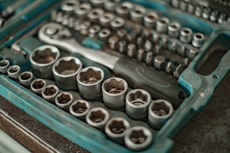 A close-up view of a socket wrench set with various socket sizes arranged neatly in a molded plastic case. The metal sockets have a shiny appearance, and the case is primarily blue with a textured surface.