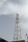 A tall metal communication tower equipped with numerous satellite dishes and antennas stands against a backdrop of a cloudy sky. The structure is intricate, composed of lattice frameworks that provide support and stability.