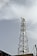 A tall metal communication tower equipped with numerous satellite dishes and antennas stands against a backdrop of a cloudy sky. The structure is intricate, composed of lattice frameworks that provide support and stability.